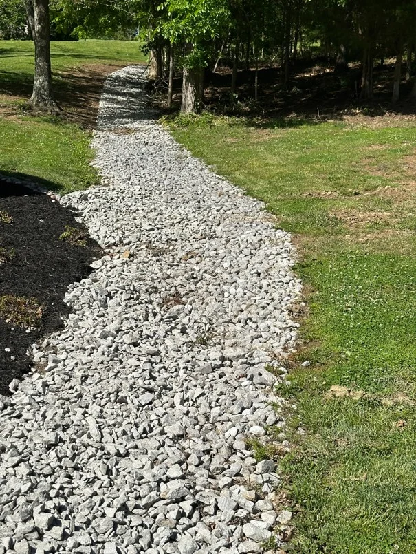 Crushed white stone drainage pathway through grassy lot with mature trees