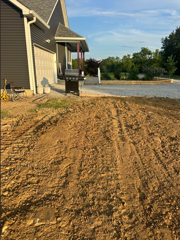 Graded dirt driveway base with compacted earth material next to residential home