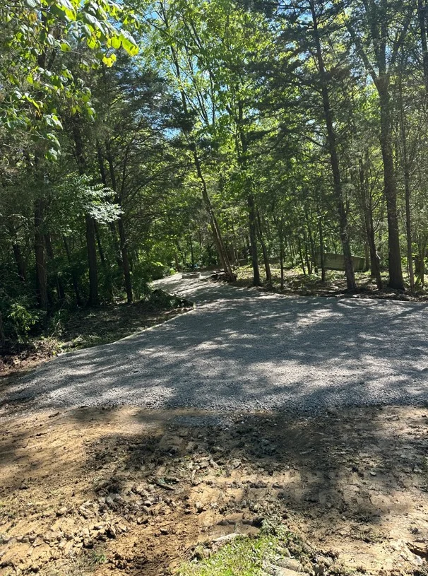 Gravel driveway through wooded area with mature trees and cleared grading