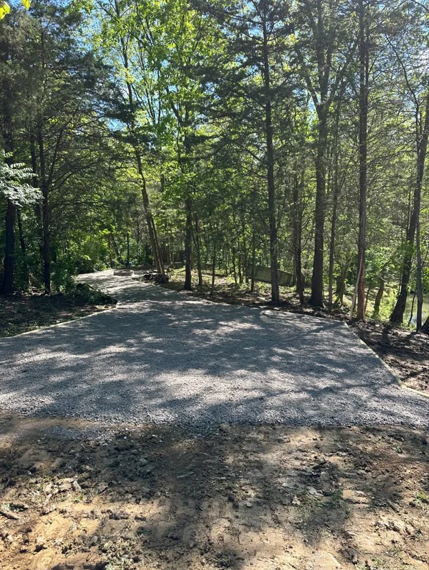 Gravel driveway through wooded area with mature trees lining both sides