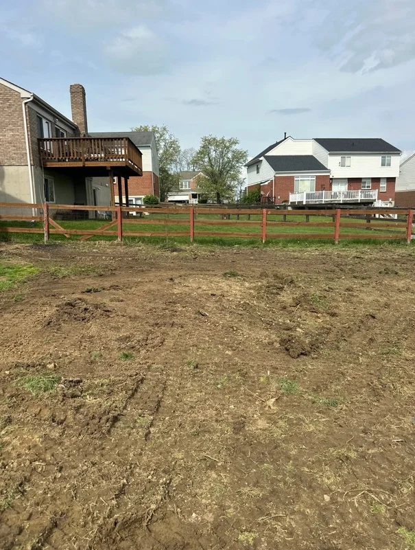 Graded dirt lot with wooden rail fence and residential homes in background