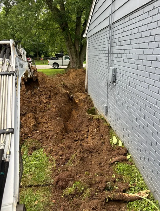 Excavated soil grading work between brick house and metal fence with heavy equipment