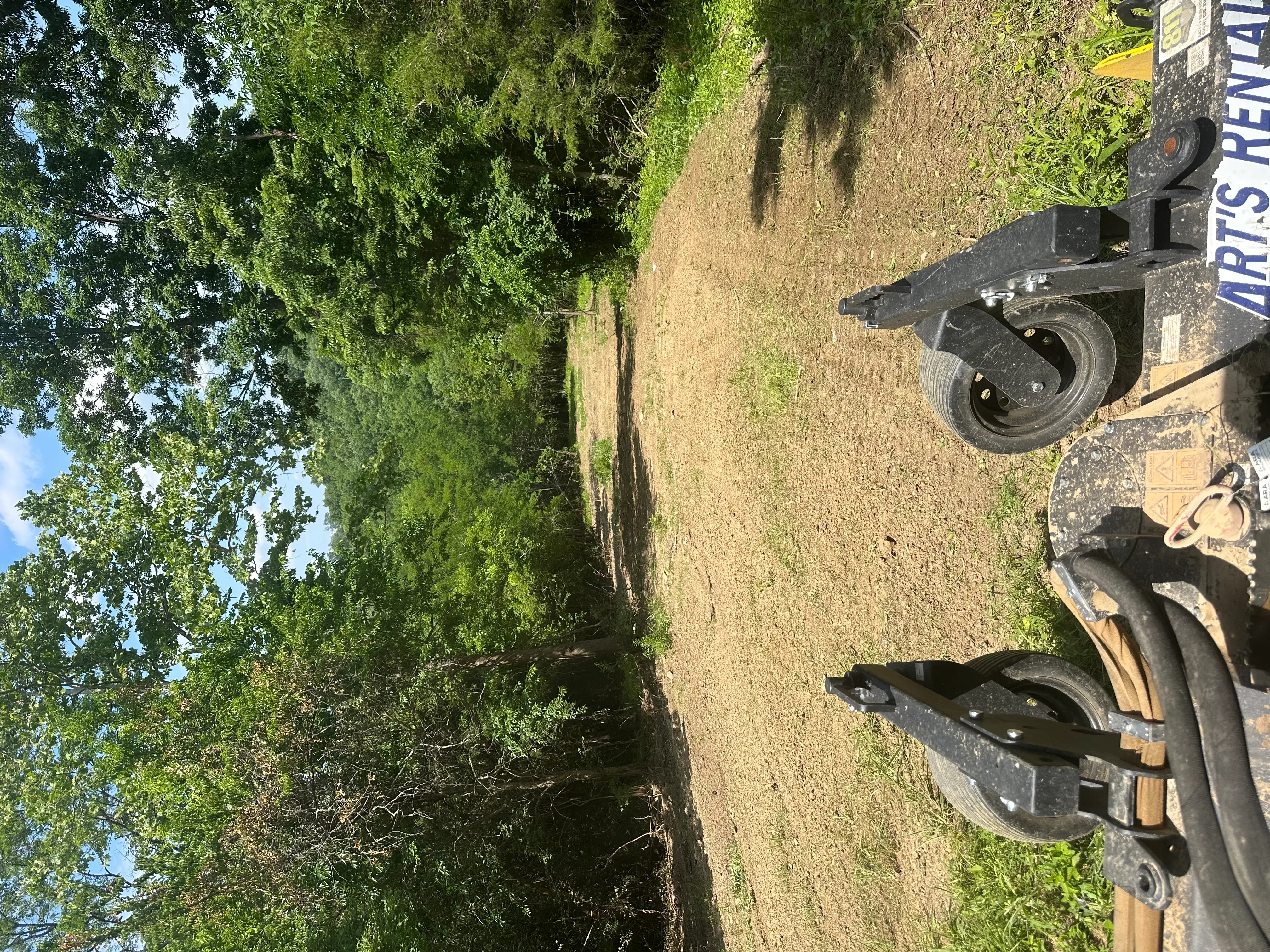 Excavation equipment on prepared dirt driveway with graded surface and surrounding vegetation