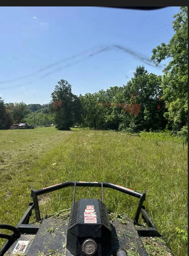 Cleared grassy field with heavy equipment, tree line in background
