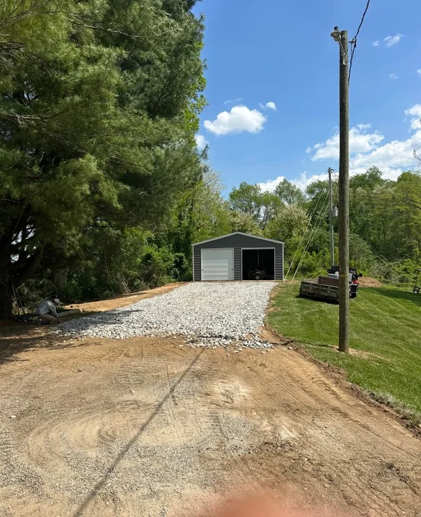 Gravel driveway with compacted stone base leading to metal garage building