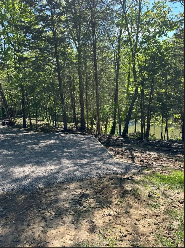 Gravel driveway through wooded area with mature trees and cleared grading