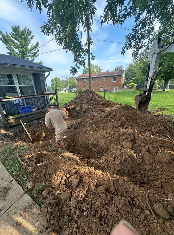Excavation work with heavy equipment moving soil at residential property, dirt pile visible
