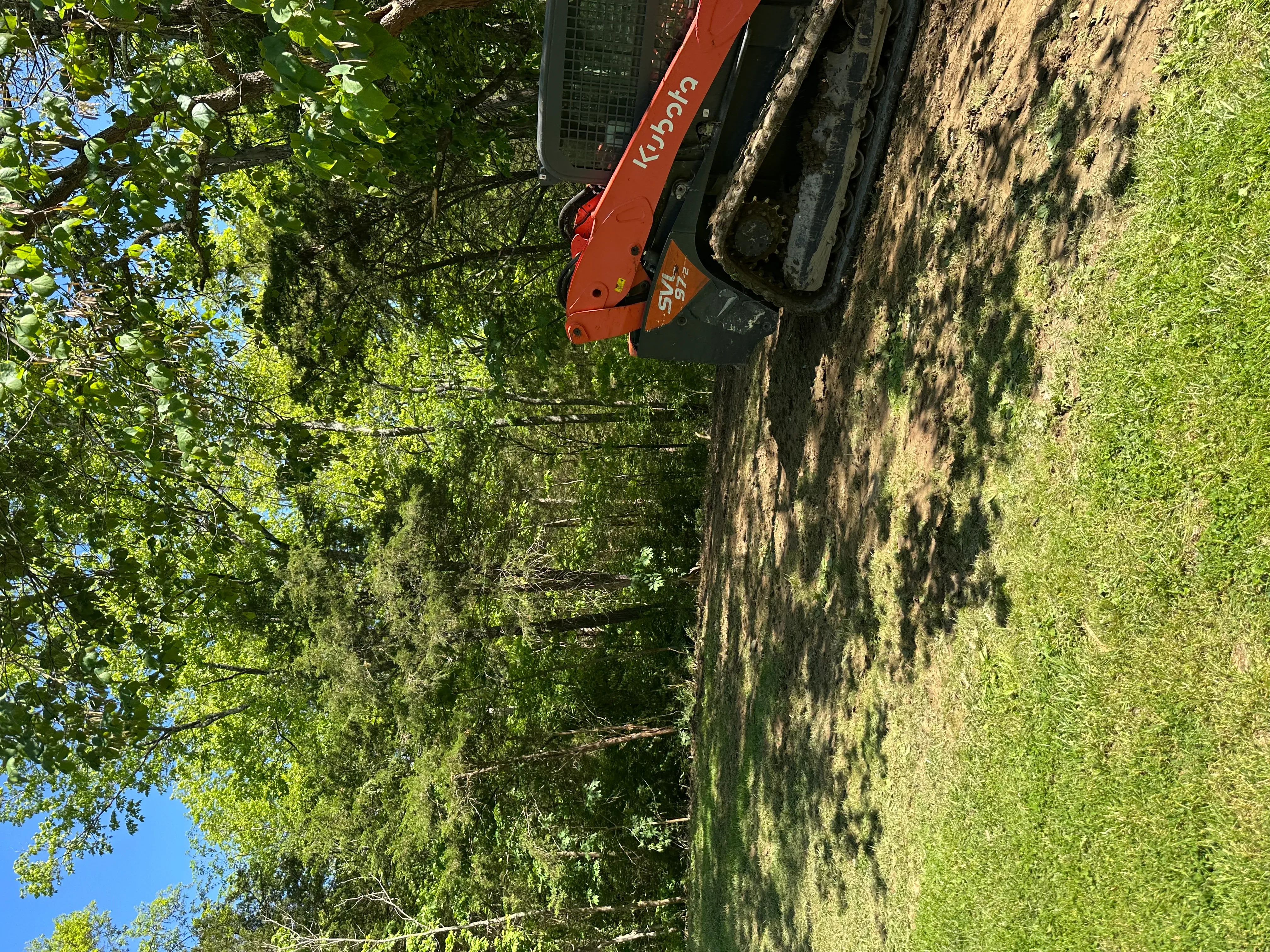 Red Kubota excavator on residential lot with cleared earth and surrounding green vegetation