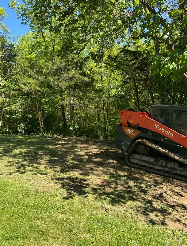 Kubota track loader on cleared lot with mature trees, fresh grading work visible