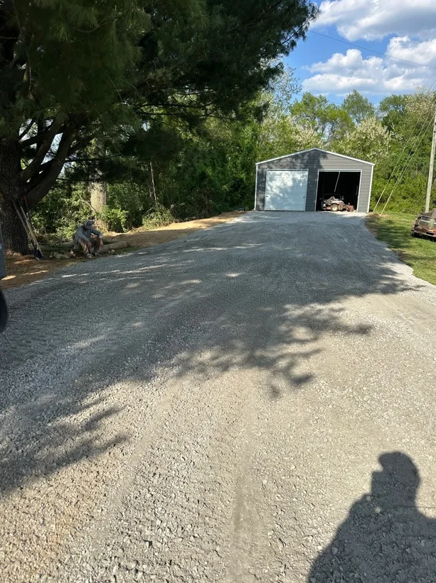 Newly installed gravel driveway with compacted stone surface leading to metal storage building
